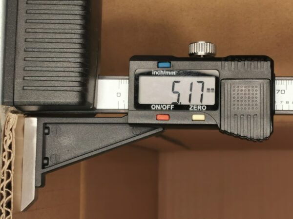 Digital caliper showing 51.1 mm measurement, jaws around a piece of cardboard.