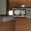 Close-up of a digital caliper reading about 7.97 mm, with the knurled thumb wheel and measurement scale visible.