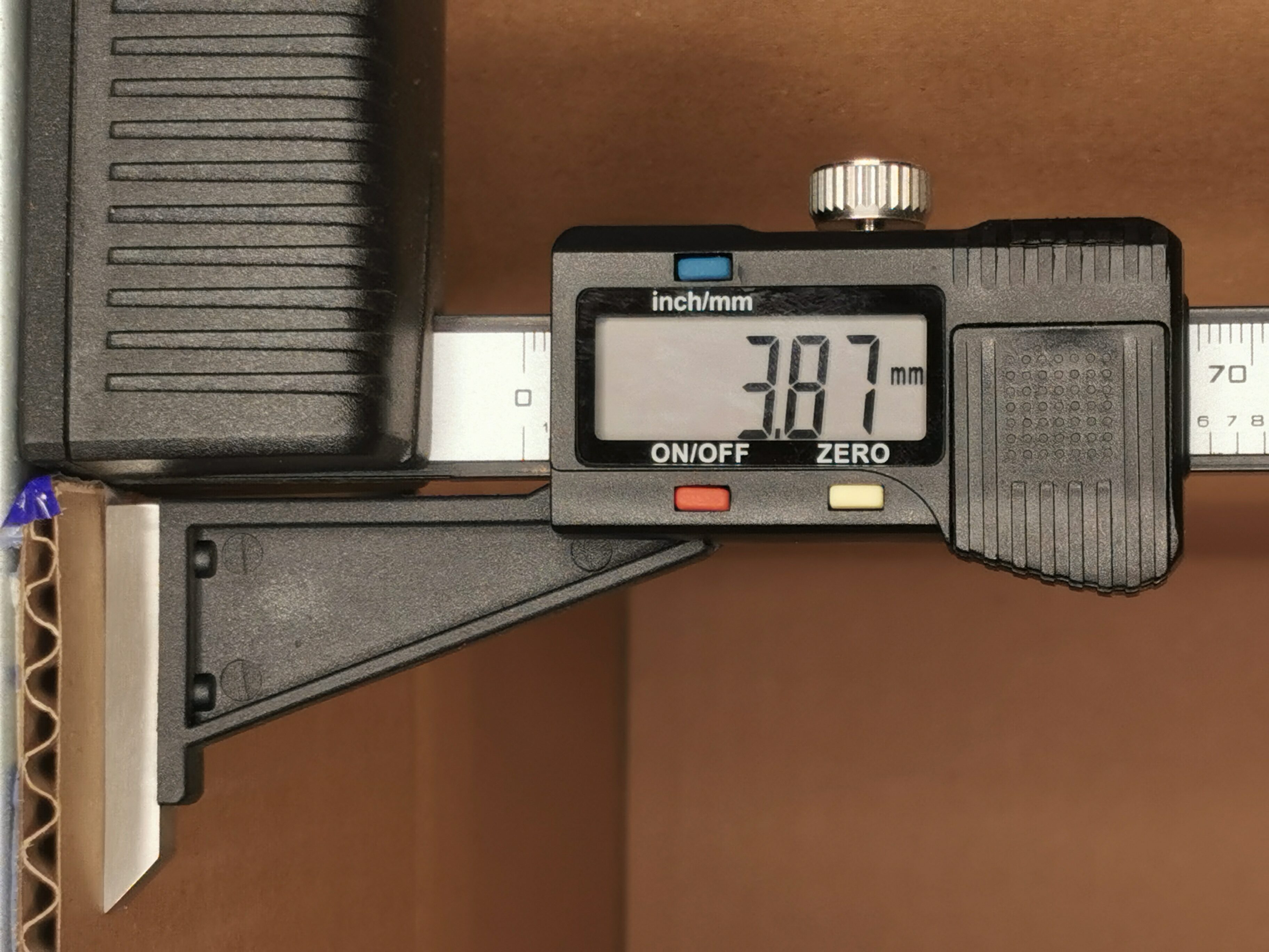 Close-up of a digital caliper reading about 7.97 mm, with the knurled thumb wheel and measurement scale visible.