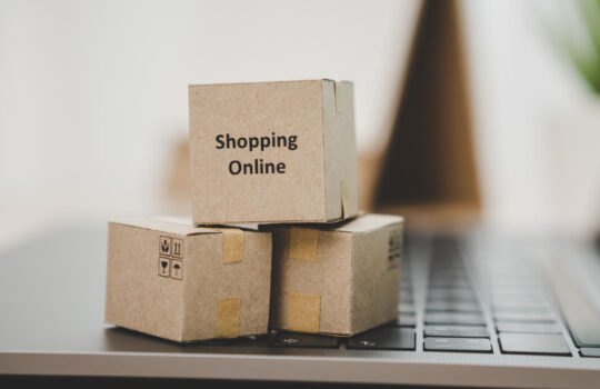 Stack of cardboard boxes on a laptop keyboard, with 'Shopping Online' printed on the top box.