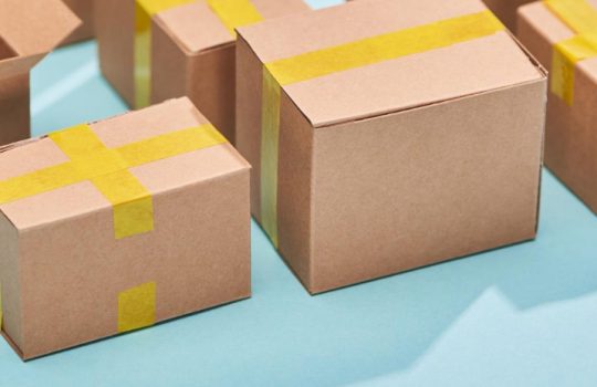 Several brown cardboard boxes sealed with yellow tape on a light blue background, suggesting shipping or gifts.